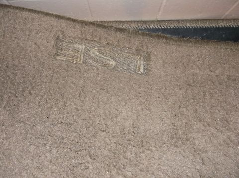 1999 Mercury Grand Marquis - A close-up of a tan floor mat with the embossed text "LSE" visible. The mat appears to be in a vehicle's interior, with a dark edge and a w…