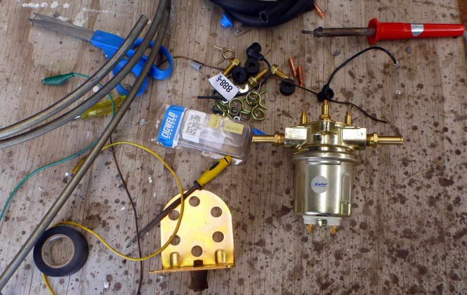 Carter electric fuel pump with brass fittings, gold mounting bracket, and hardware laid out on a workbench