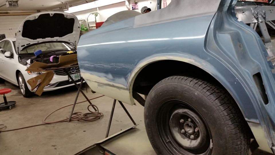 Photo of a blue car body and wheel on a stand in a shop