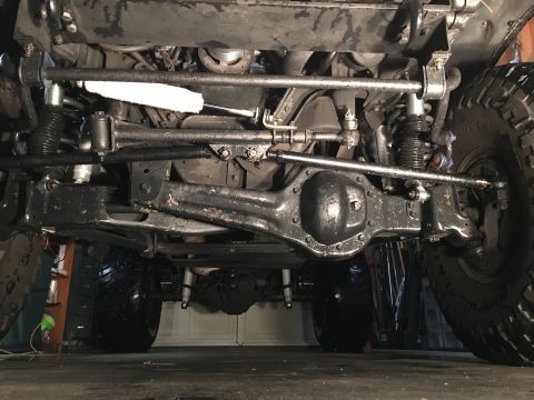 1993 Ford Bronco - The underside of a 1993 Ford Bronco is shown, focusing on the front axle, steering components, and suspension. The vehicle is in a garage s…