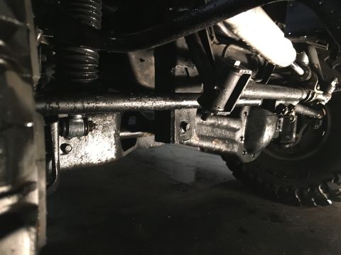1993 Ford Bronco - The underside of a vehicle, likely a 1993 Ford Bronco, shows the front axle, steering components, and suspension. The parts are heavily coa…