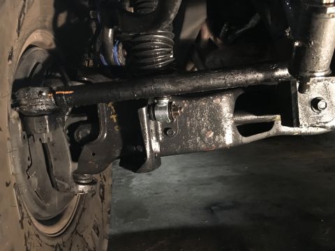 1993 Ford Bronco - A close-up, low-angle view of the front suspension and steering components of a vehicle, likely a 1993 Ford Bronco, showing a heavily greas…