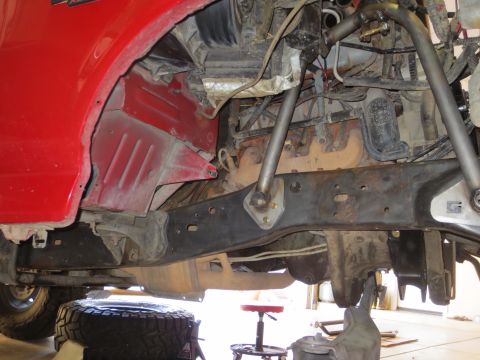 1996 Ford Bronco - The underside of a red 1996 Ford Bronco shows the suspension and frame components, with a tire resting on the ground below.