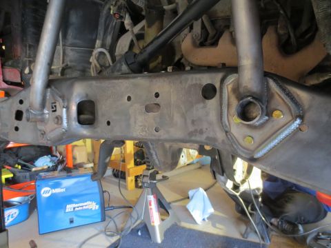 1996 Ford Bronco - A close-up view of the heavily modified frame of a 1996 Ford Bronco, showing custom welding and reinforcement brackets. A Miller welding ma…