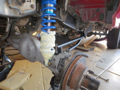 1996 Ford Bronco - The underside of a vehicle is shown, focusing on the suspension system. A blue coilover shock absorber is visible, wrapped in white tape, a…
