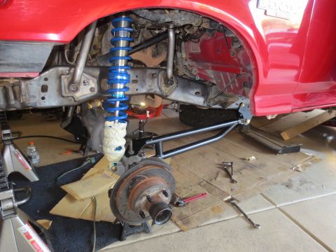 1996 Ford Bronco - The front suspension of a red Ford Bronco is shown disassembled, with the coilover shock and brake rotor visible. The vehicle is supported…