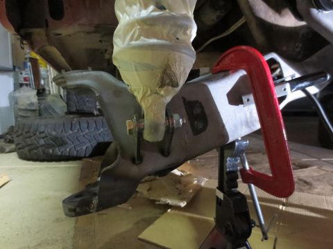1996 Ford Bronco - A metal bracket, possibly part of a suspension system, is being held in place with a red C-clamp and a black jack stand. The bracket is cov…