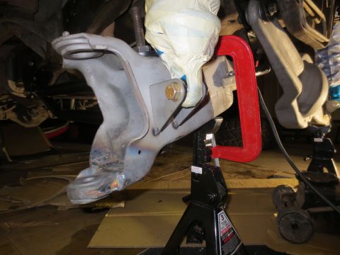 1996 Ford Bronco - A close-up view of a vehicle's suspension components, held in place by a red C-clamp and supported by jack stands. Welds are visible on the…