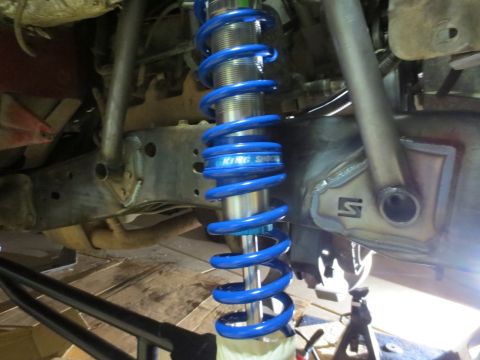 1996 Ford Bronco - A close-up view of a blue coilover shock absorber mounted to the undercarriage of a vehicle, likely a 1996 Ford Bronco. The shock is brande…