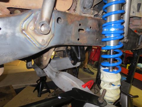 1996 Ford Bronco - Close-up view of the front suspension components of a 1996 Ford Bronco, showing a newly welded bracket on the frame and a bright blue coilo…