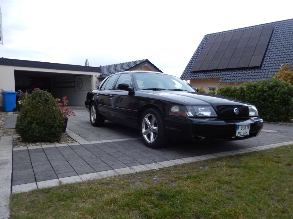 Black Mercury sedan parked in driveway with garage and house in background.