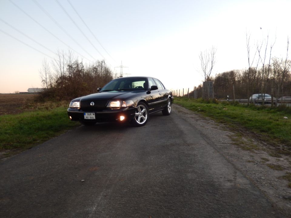 Black Mercury Marauder parked on a rural road at dusk, headlights on.
