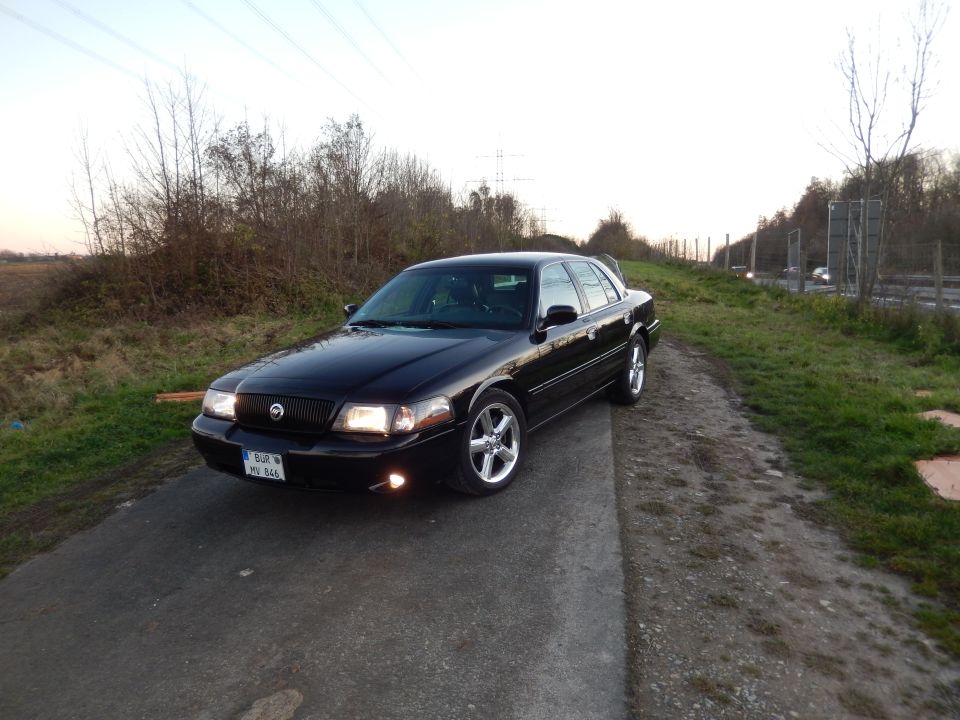 Black 2003 Mercury Marauder parked on a dirt path, headlights on.