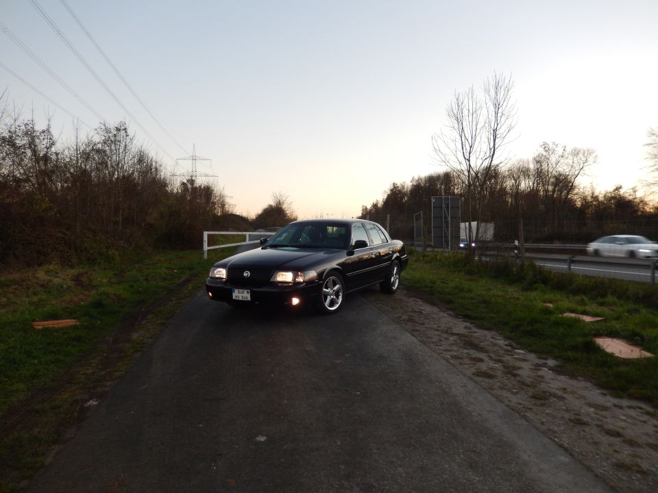 Black 2003 Mercury Marauder with headlights on, parked on a paved path.
