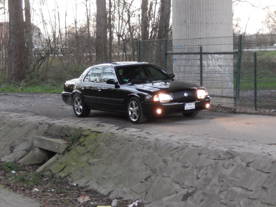 Black 2003 Mercury Marauder with illuminated headlights parked outdoors.