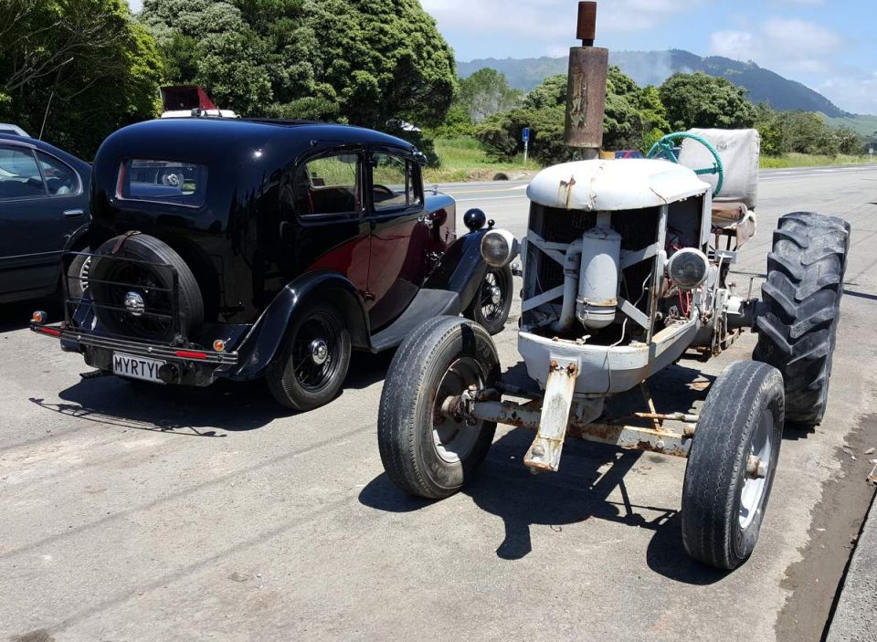 Vintage black sedan next to a weathered tractor with a tall exhaust pipe.