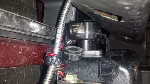1996 Ford Bronco - A close-up view of a black electronic component with visible text, possibly a sensor or control module, mounted on a vehicle. A braided met…