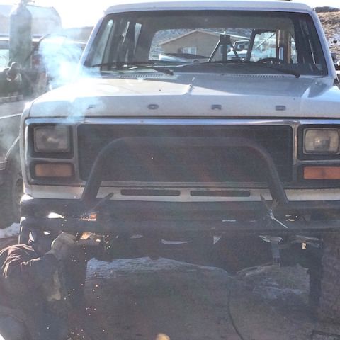 1981 Ford Bronco - A person is welding on the front bumper of a white Ford Bronco, creating sparks and smoke. The vehicle appears to be undergoing modificatio…