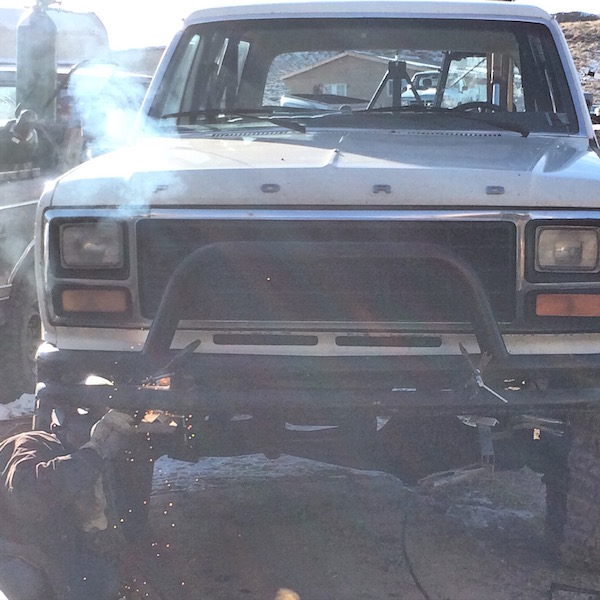 White Ford Bronco with a person welding on the front bumper, creating sparks and smoke.