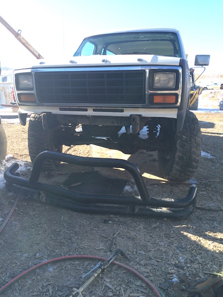 1981 Ford Bronco - A white 1980s Ford Bronco is parked outdoors with a black brush guard lying on the ground in front of it. The front grille and headlights a…