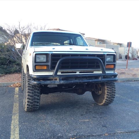 1981 Ford Bronco - Front view of a lifted white Ford Bronco with a black brush guard and aggressive off-road tires parked in a paved lot.