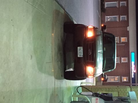 1991 Ford Bronco - A dark colored Ford van is parked in front of a brick building with multiple windows. The van's headlights and amber marker lights are illu…
