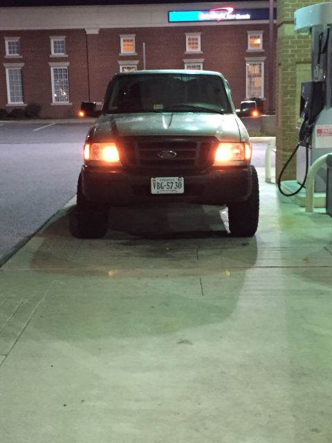 1991 Ford Bronco - A dark-colored Ford pickup truck is parked at a gas station at night, with its headlights illuminated. The truck has a Virginia license pla…