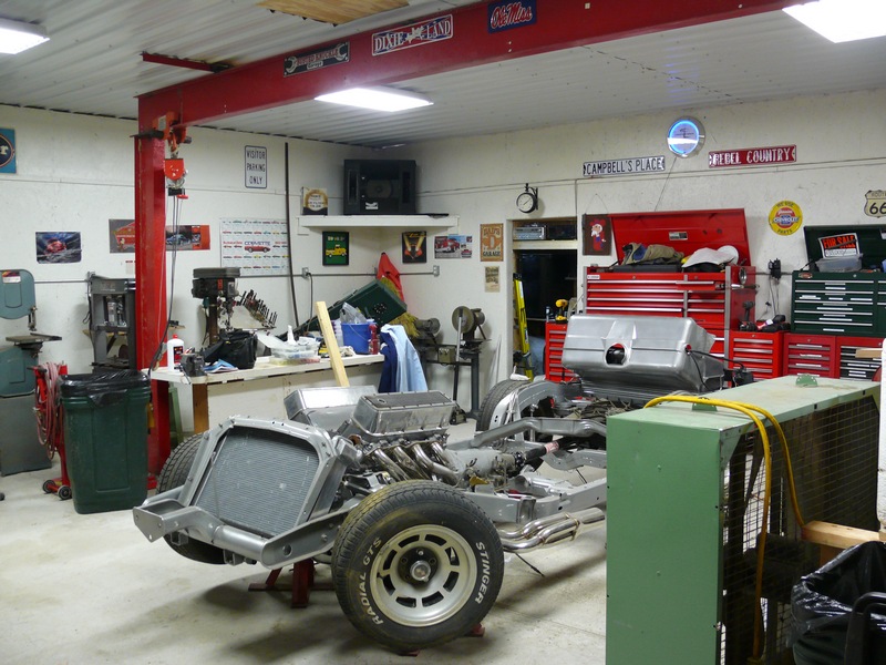 Car chassis with engine and suspension in a garage with tools and decorations.