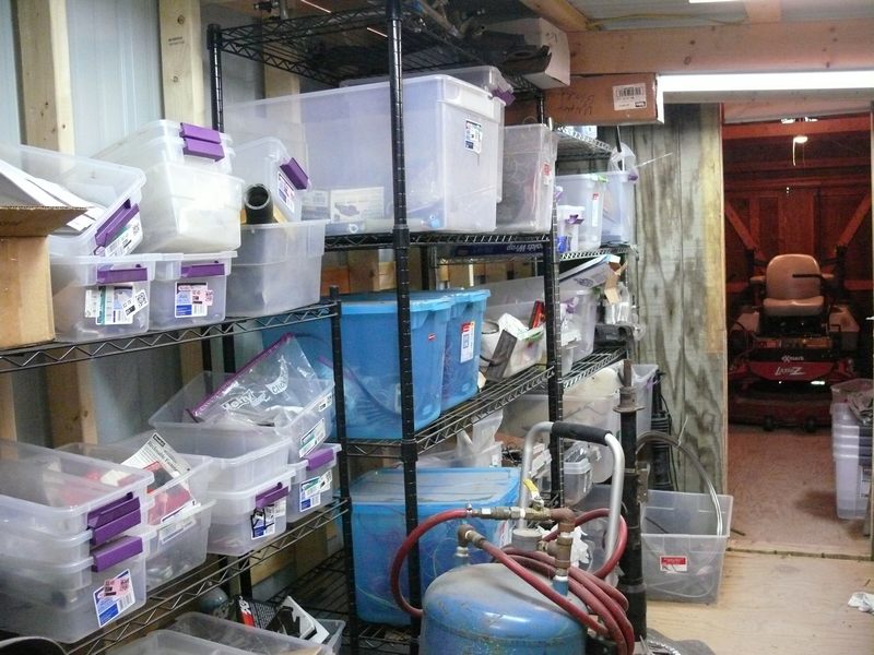 Storage room with shelves of bins and a riding lawn mower in the background.