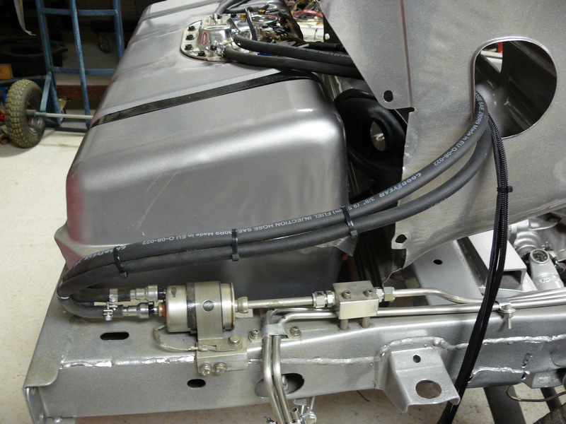 Gray fuel tank with black fuel lines and a fuel filter mounted to a vehicle chassis.