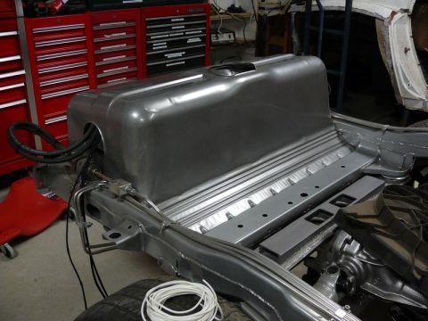 Custom aluminum fuel tank installed in vehicle chassis with metal lines and hoses connected.