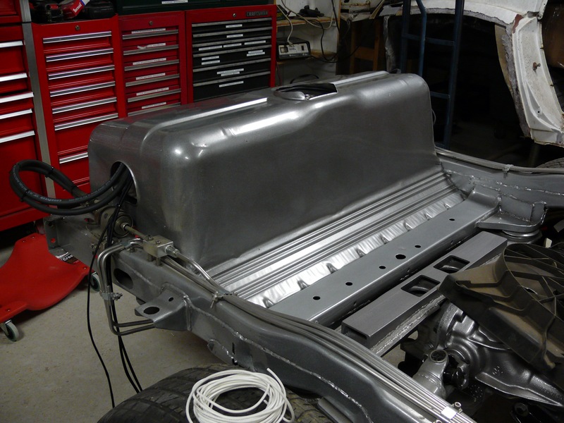 Custom aluminum fuel tank installed in vehicle chassis with metal lines and hoses connected.