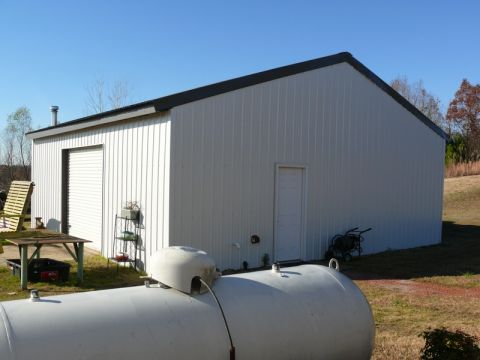 Large white propane tank in front of a white metal building with a garage door.