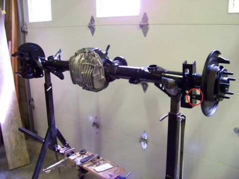 1999 Mercury Grand Marquis - A rear axle assembly, likely from a 1999 Mercury Grand Marquis, is mounted on two black stands in a garage. The assembly features a differe…