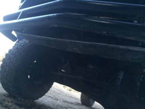 1981 Ford Bronco - A low-angle, close-up view of the front bumper and tire of a dark-colored vehicle, likely an off-road SUV, with a rugged tire tread visible.
