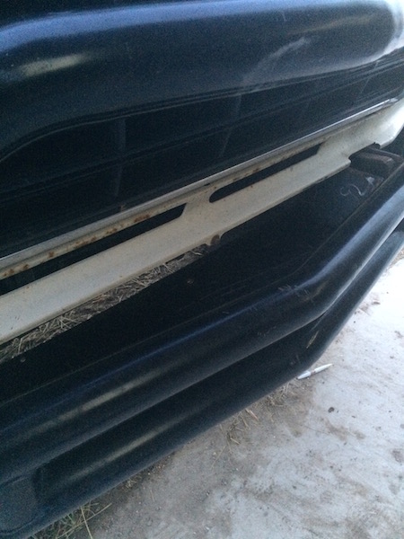1981 Ford Bronco - A close-up, low-angle view of the front bumper and grille area of a dark-colored vehicle, possibly a Ford Bronco, showing a white metal sup…