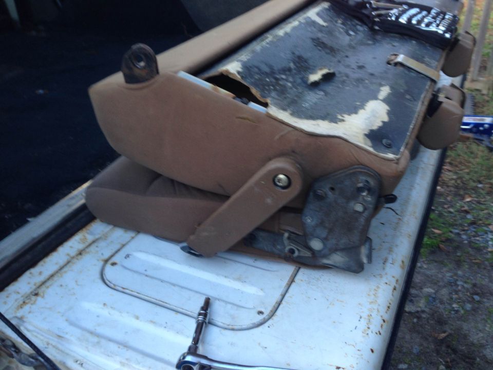 Disassembled tan car seat on a rusty white truck bed with a socket wrench.