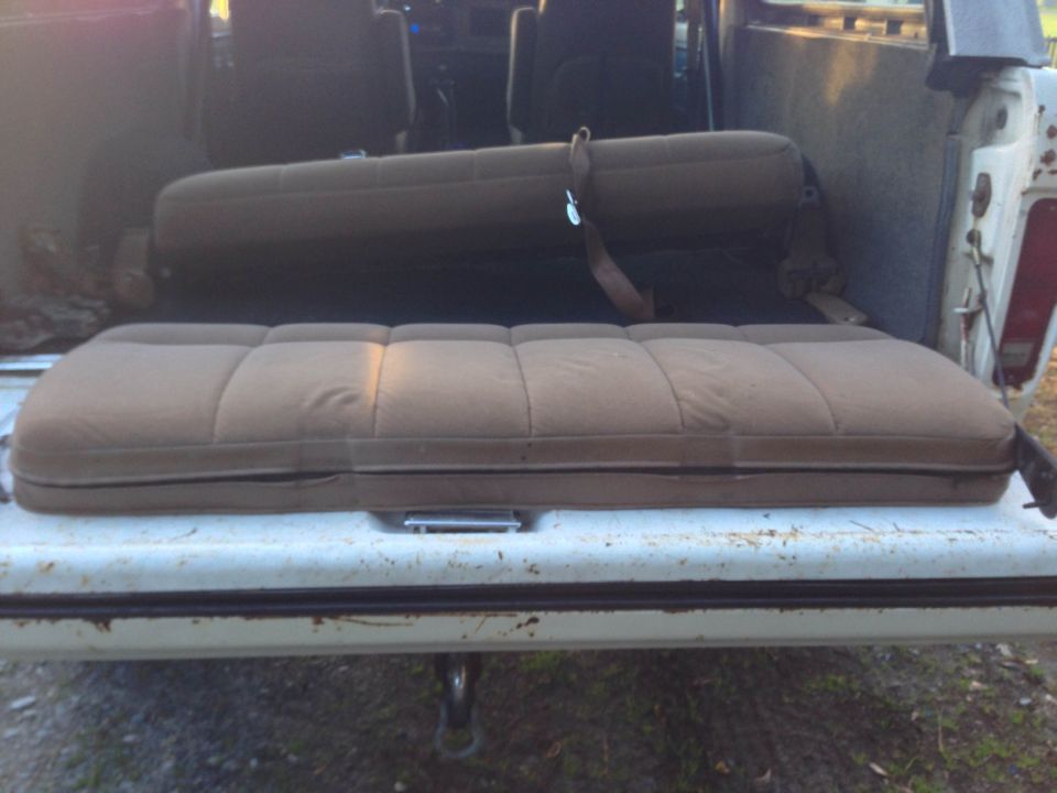 Two brown upholstered seats inside a vehicle, one folded, one flat on the tailgate.