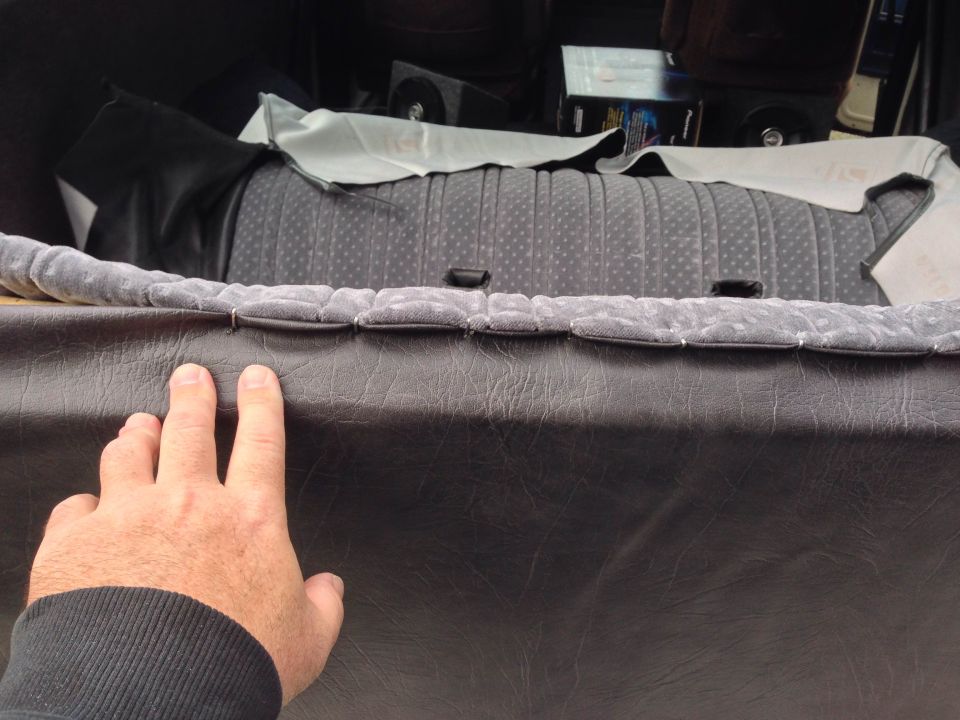Hand pressing on dark gray vinyl panel with gray patterned seat behind.