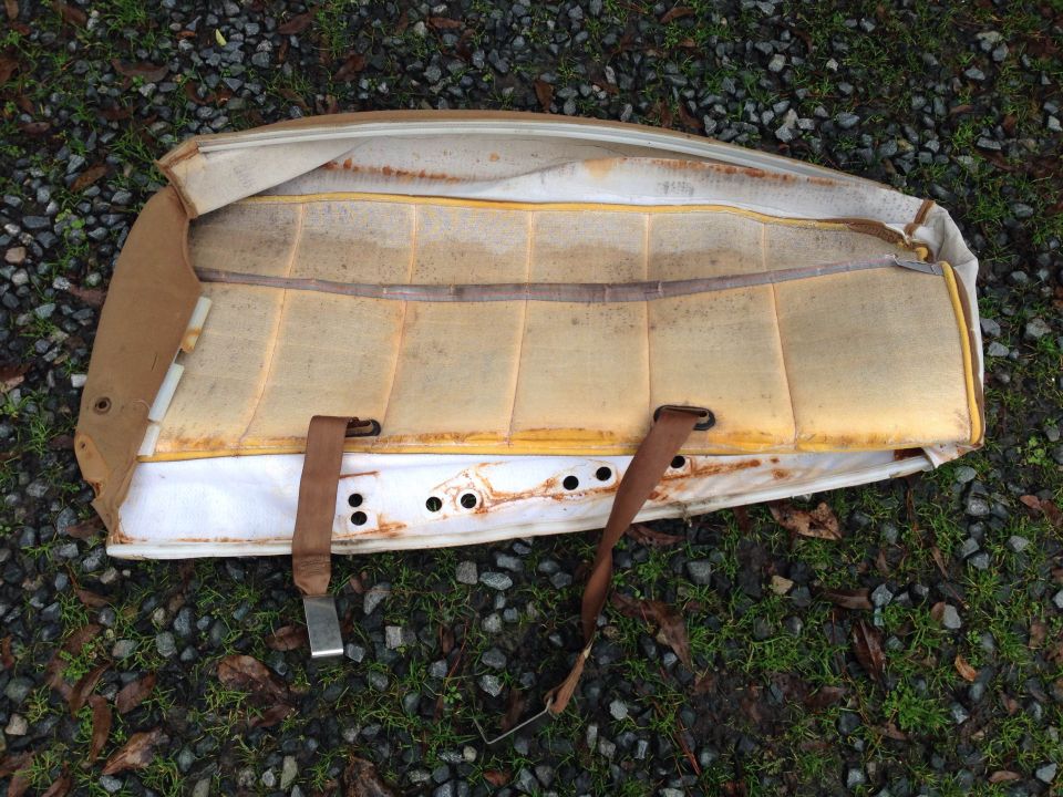 Underside of a tan car seat cushion with exposed foam and a brown seatbelt strap.
