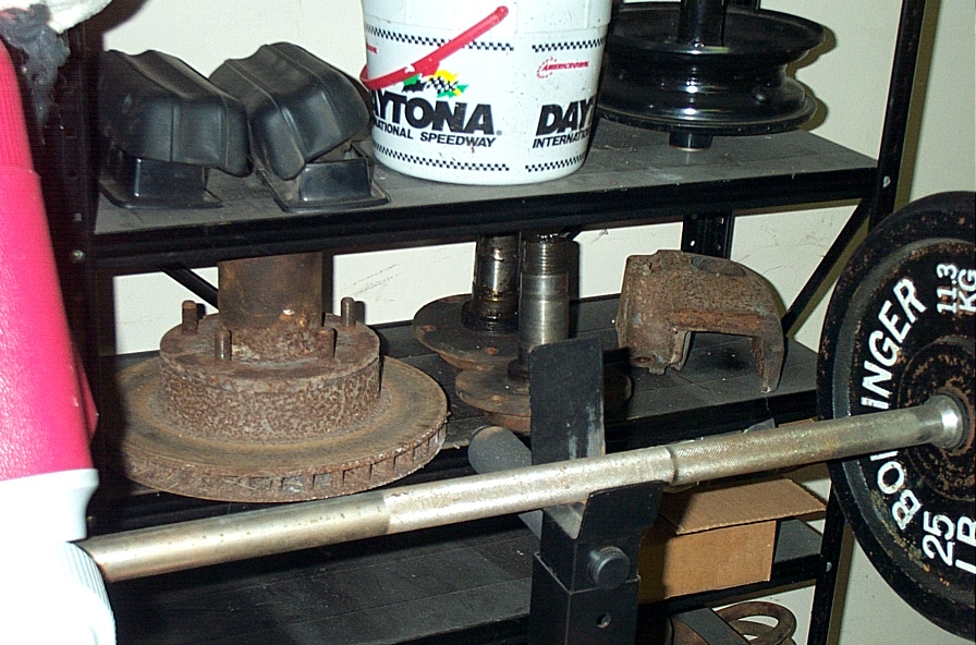 Rusty brake rotor, hubs and steering knuckle stored on a garage shelf