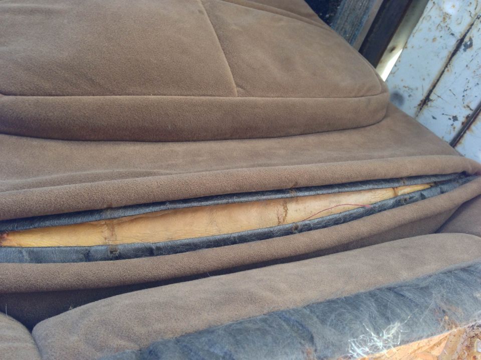 Torn brown vehicle seat showing yellow foam and black fabric.