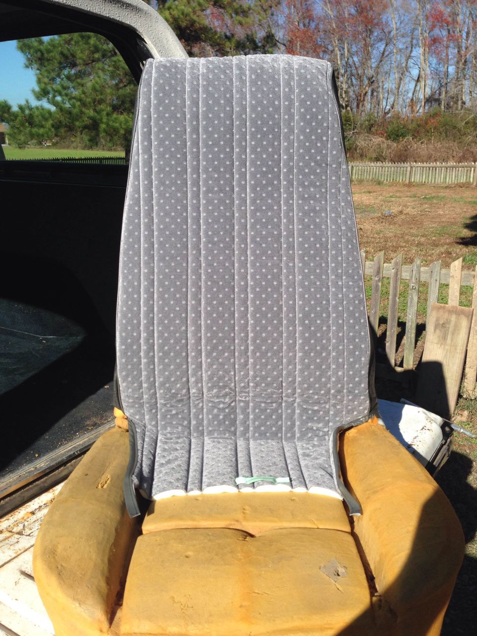 Gray velour car seat with white polka dots and exposed yellow foam, viewed from the front