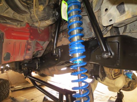 1996 Ford Bronco - The underside of a vehicle shows a bright blue King coilover shock absorber mounted to a black suspension component. The red painted frame…