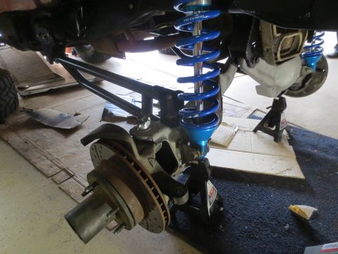 1996 Ford Bronco - The underside of a vehicle is shown, with a focus on the suspension system. A bright blue coilover shock absorber is prominently displayed,…