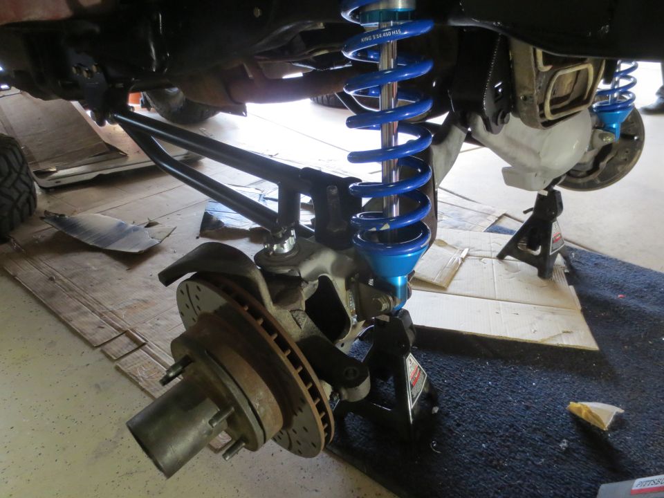 Underside of a vehicle showing suspension, blue coilover shock, brake rotor, and hub.
