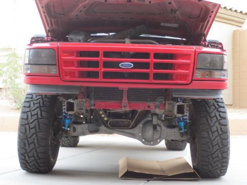 1996 Ford Bronco - Front view of a red Ford Bronco with its hood open, showing the grille, headlights, and suspension components. The vehicle is lifted with l…