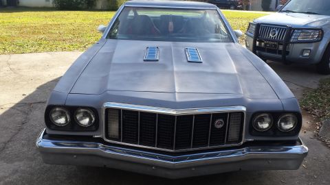 1976 Ford Ranchero - Front view of a gray 1976 Ford Ranchero with chrome accents on the grille and bumper. The vehicle has two hood scoops and is parked on a co…