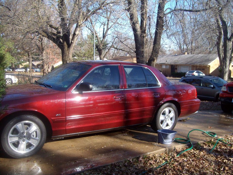 Red 2004 Ford Crown Victoria sedan parked on wet driveway with bucket and hose.
