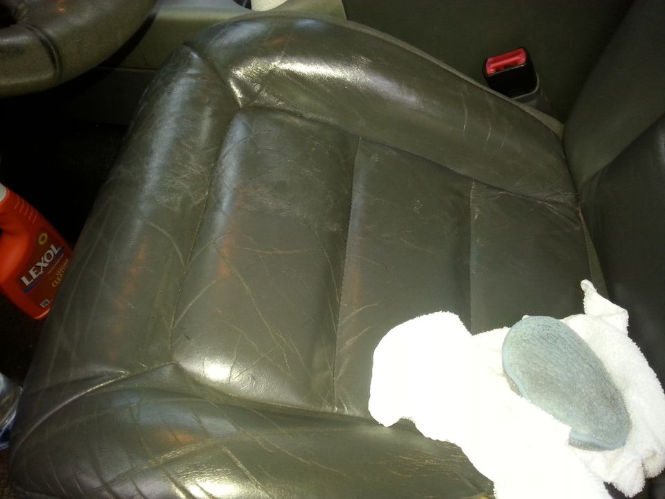Gray leather car seat with Lexol cleaner and cleaning supplies.